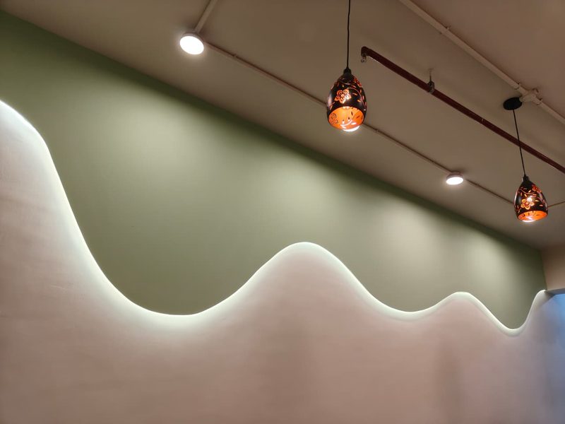 Green feature wall with a lit wave edge and hanging lamps at Twing Cafe Rajkot