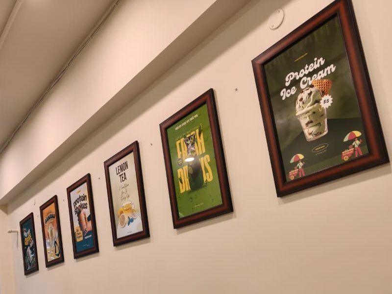 Framed Twing Cafe menu posters on the wall: protein ice cream, fresh drinks, lemon tea and protein shakes